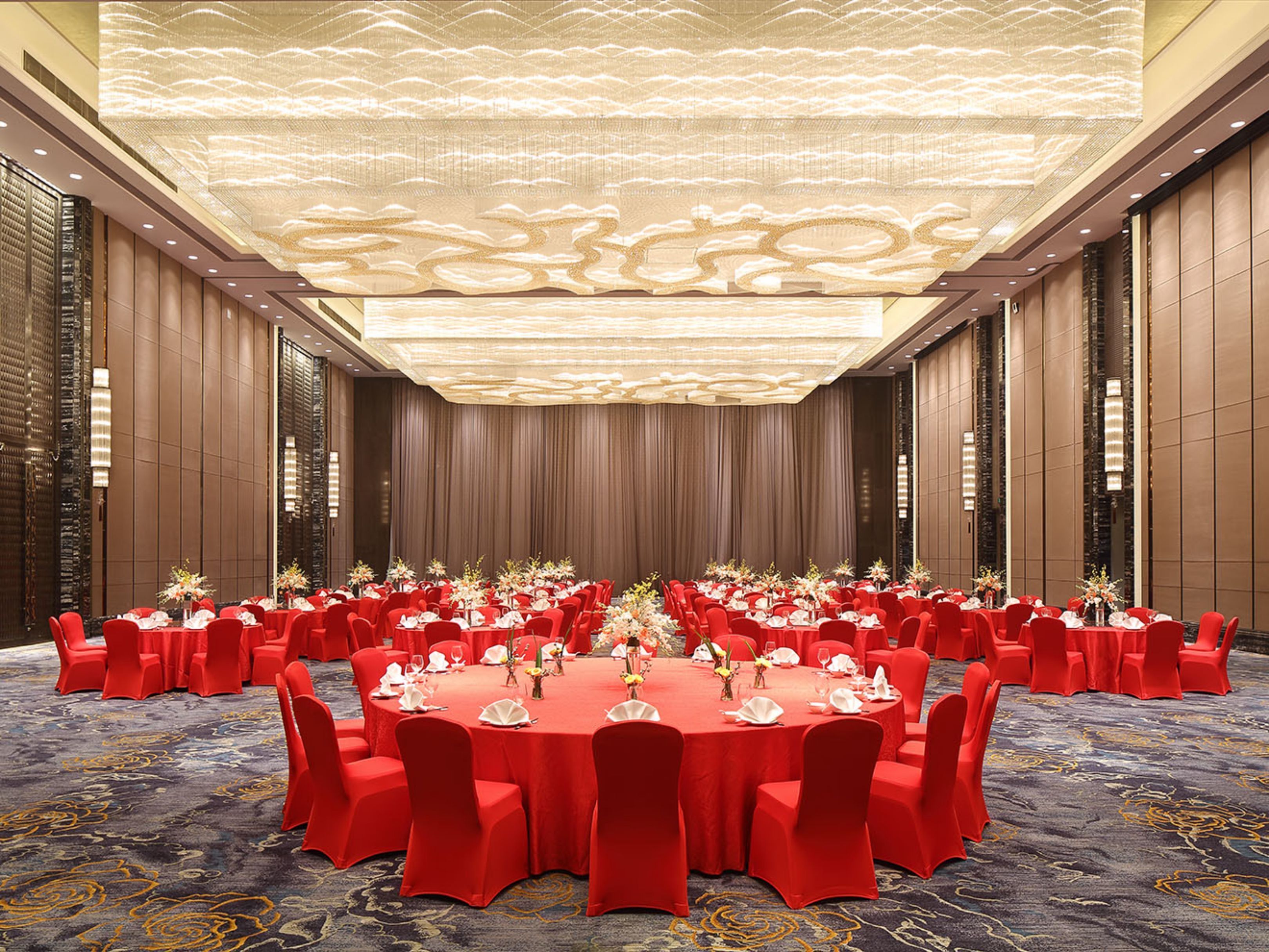 A large conference room with round tables, red chairs, and a patterned carpet.