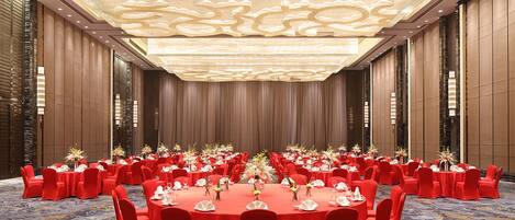A large conference room with round tables, red chairs, and a patterned carpet.