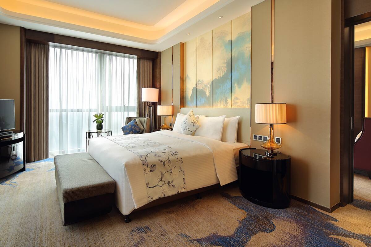 A hotel room with a large bed, bedside tables, a TV, and a view of the outdoors.