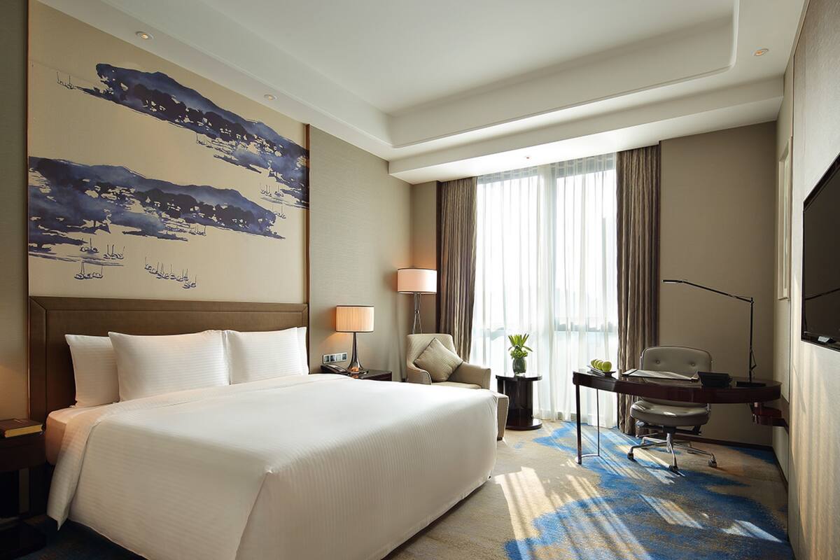 A hotel room with a large bed, a desk, a chair, a TV, and a painting on the wall.