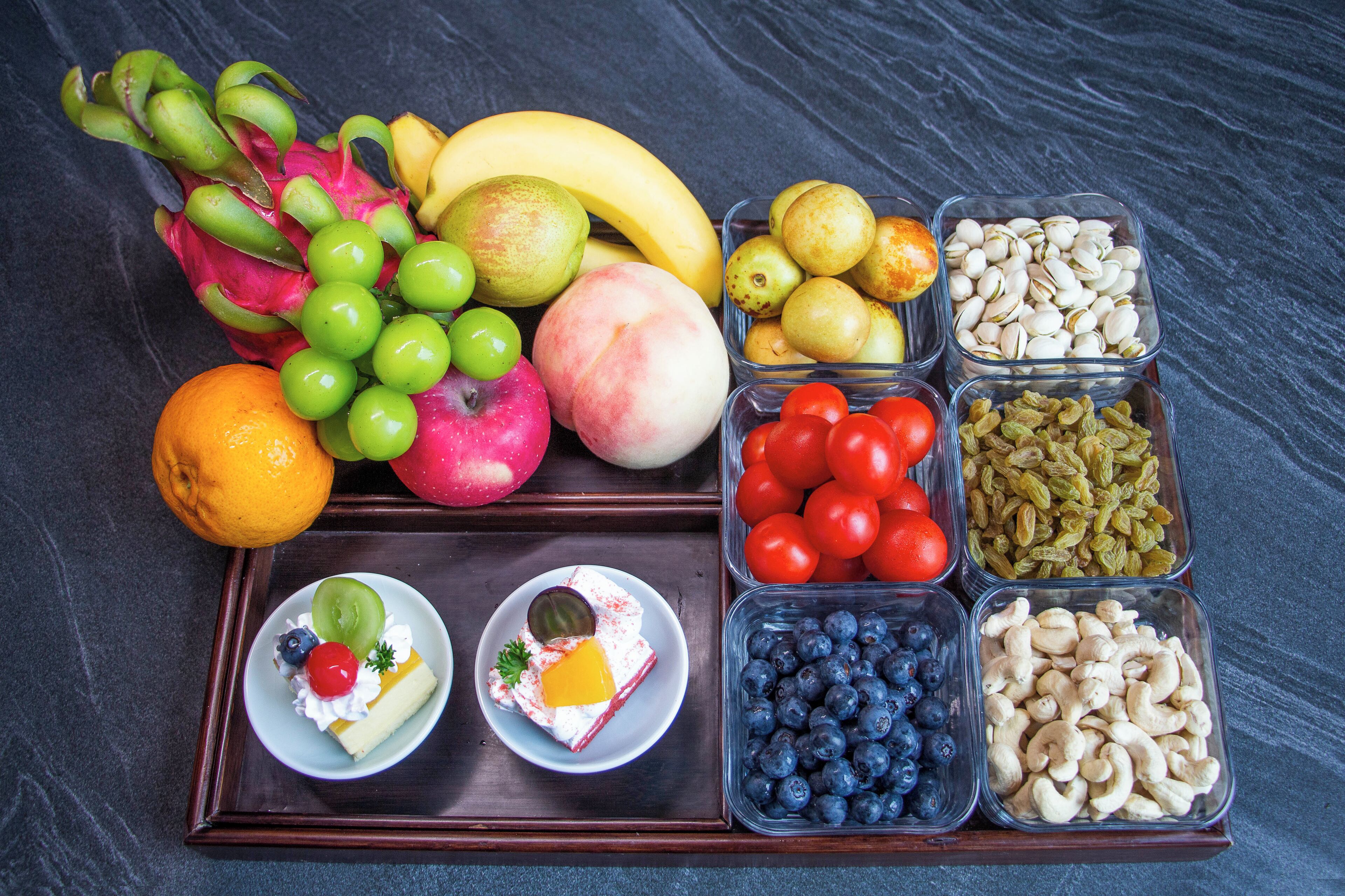 A tray of assorted fruits and nuts, including dragon fruit, bananas, apples, and cashews.