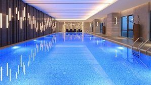 Una piscina interior moderna con suelo de mosaico azul, un amplio pasillo con vistas y luminarias contemporáneas.