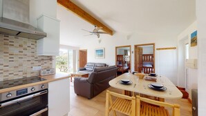 A modern kitchen with a built-in oven and a dining area with a wooden table and chairs. - F26 Porthia, Riviere Towans (Hayle)