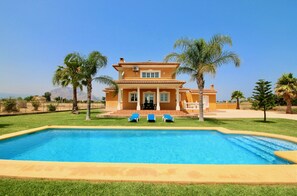 Ein zweistöckiges Haus mit Pool, umgeben von Palmen und blauem Himmel.