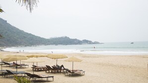 A beach with sun loungers and umbrellas, a sandy shore, and a view of the ocean and hills in the background. - Ramsons Resort (Canacona)