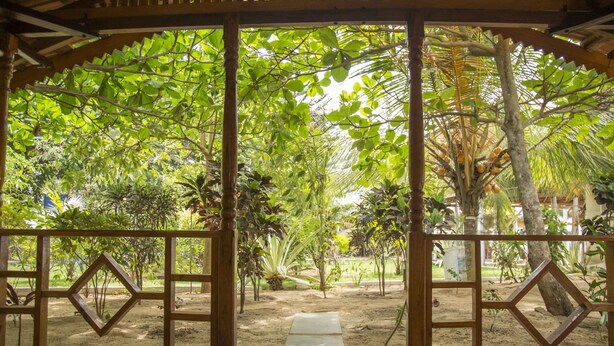 A wooden gate with a welcome mat leading to a garden with various plants and trees. - Ramsons Resort (Canacona)