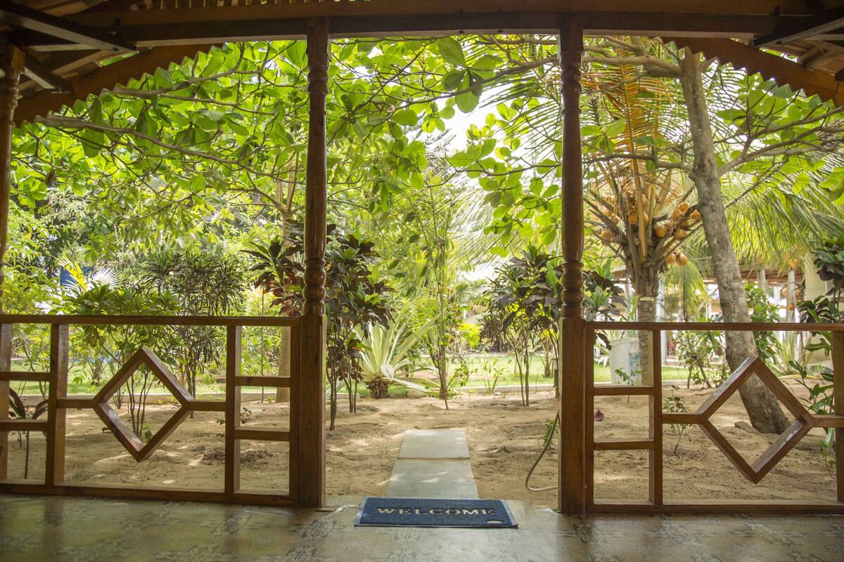 A wooden gate with a welcome mat leading to a garden with various plants and trees.