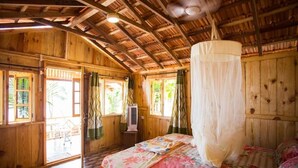 A wooden cabin with a bed, a ceiling fan, and a mosquito net. - Ramsons Resort (Canacona)
