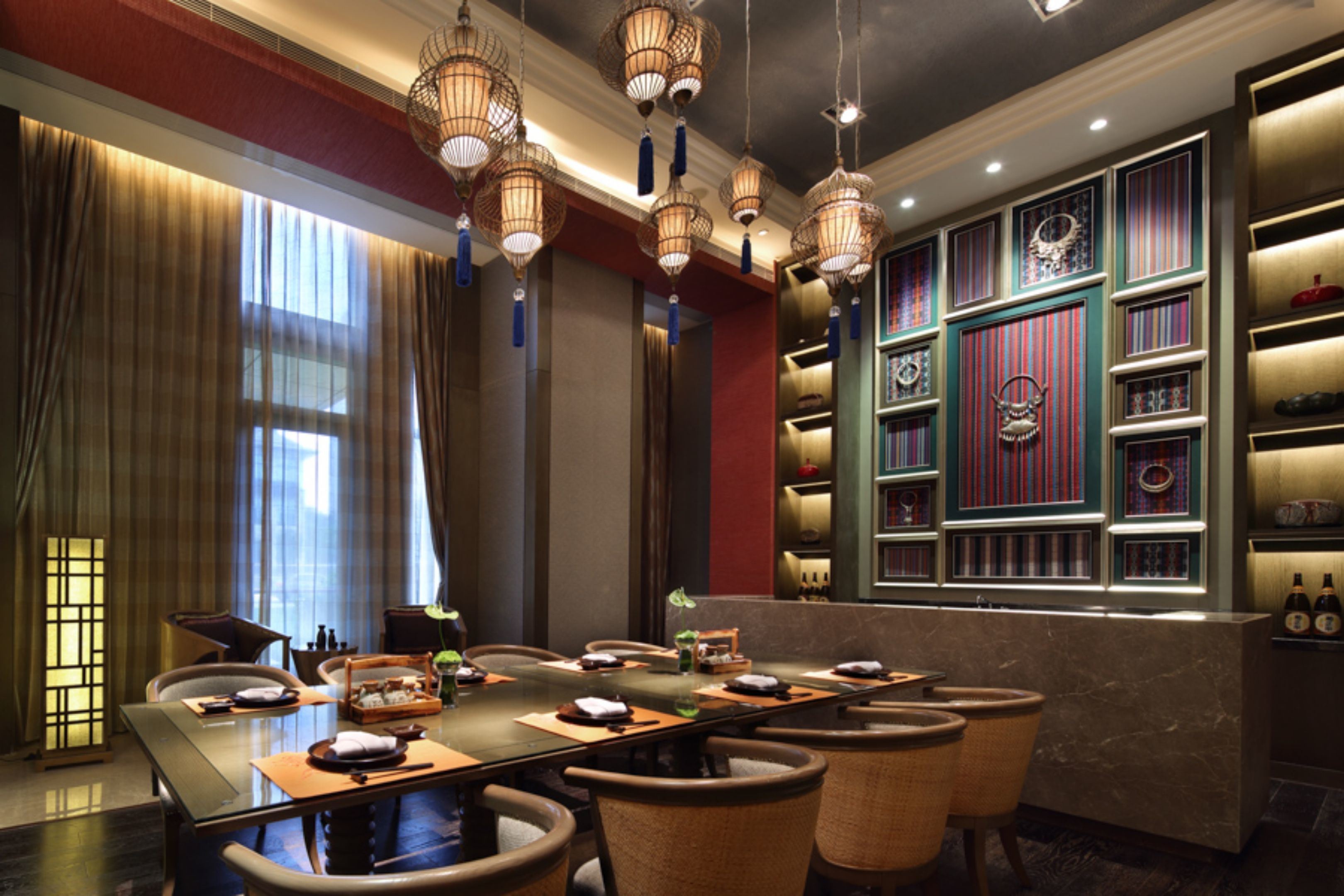Un espace repas comprenant une longue table, des chaises, des lampes suspendues et un mur décoratif agrémenté d’étagères.