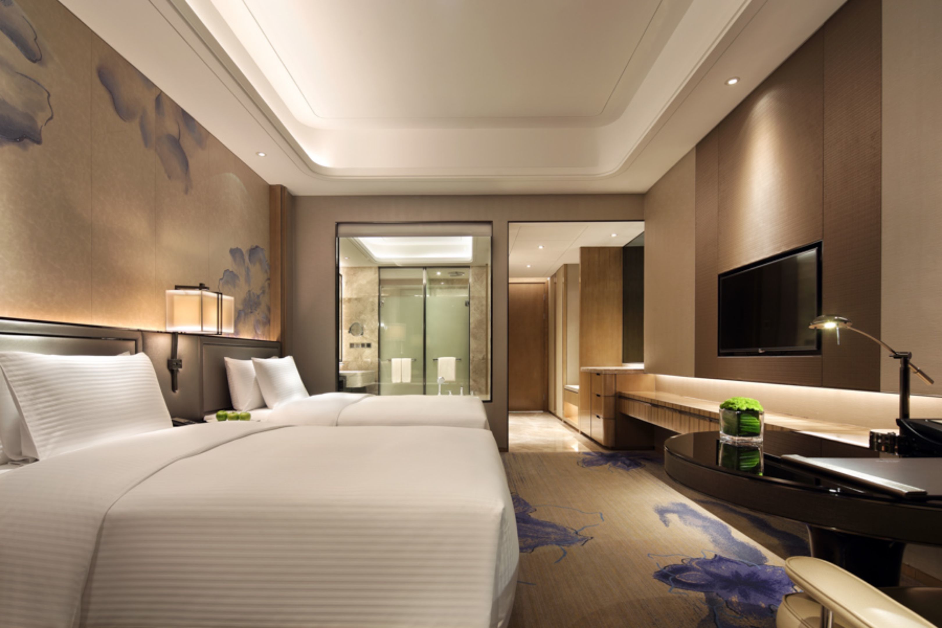 Een hotelkamer met een groot bed, een bureau, een flatscreen televisie en een badkamer zichtbaar door een glazen deur.