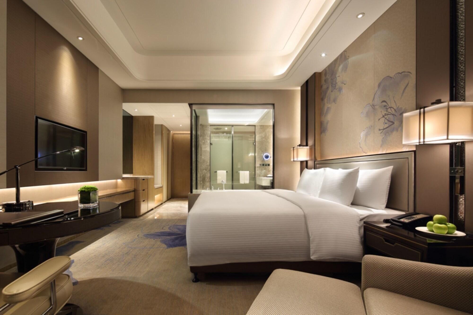 Una habitación de hotel con cama, escritorio, silla, televisión y baño visible a través de una puerta abierta.