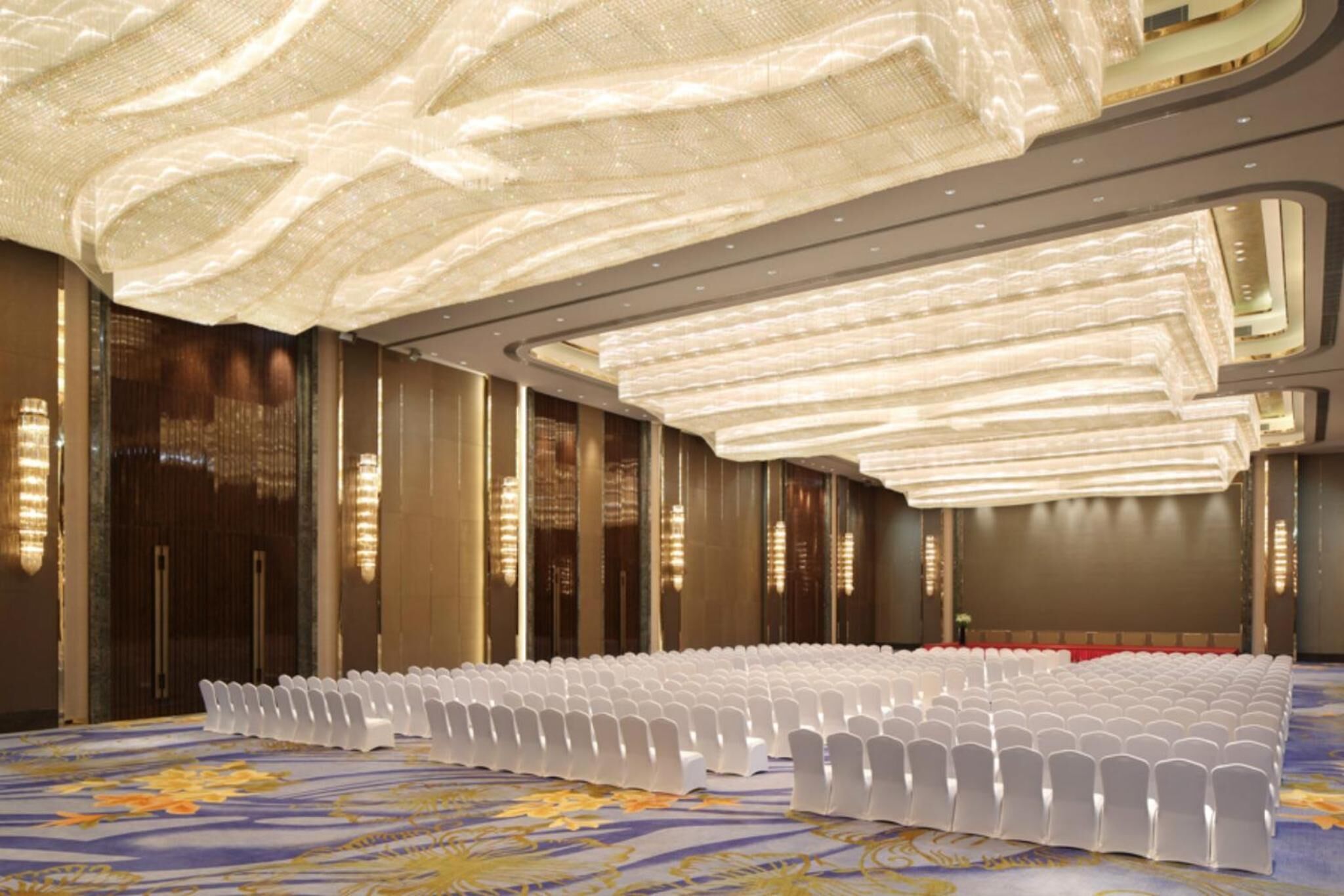 A large conference room with rows of white chairs, a patterned carpet, and a high ceiling with a unique light fixture.