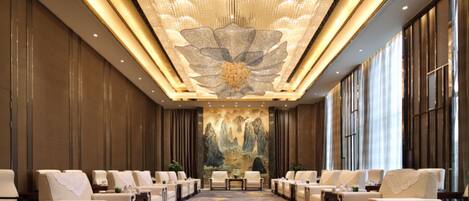 A hotel lobby with a long row of seating, a large floral ceiling design, and a mural on the wall.