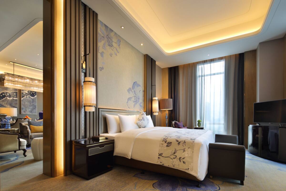A modern hotel room with a large bed, a desk, a television, and a seating area.