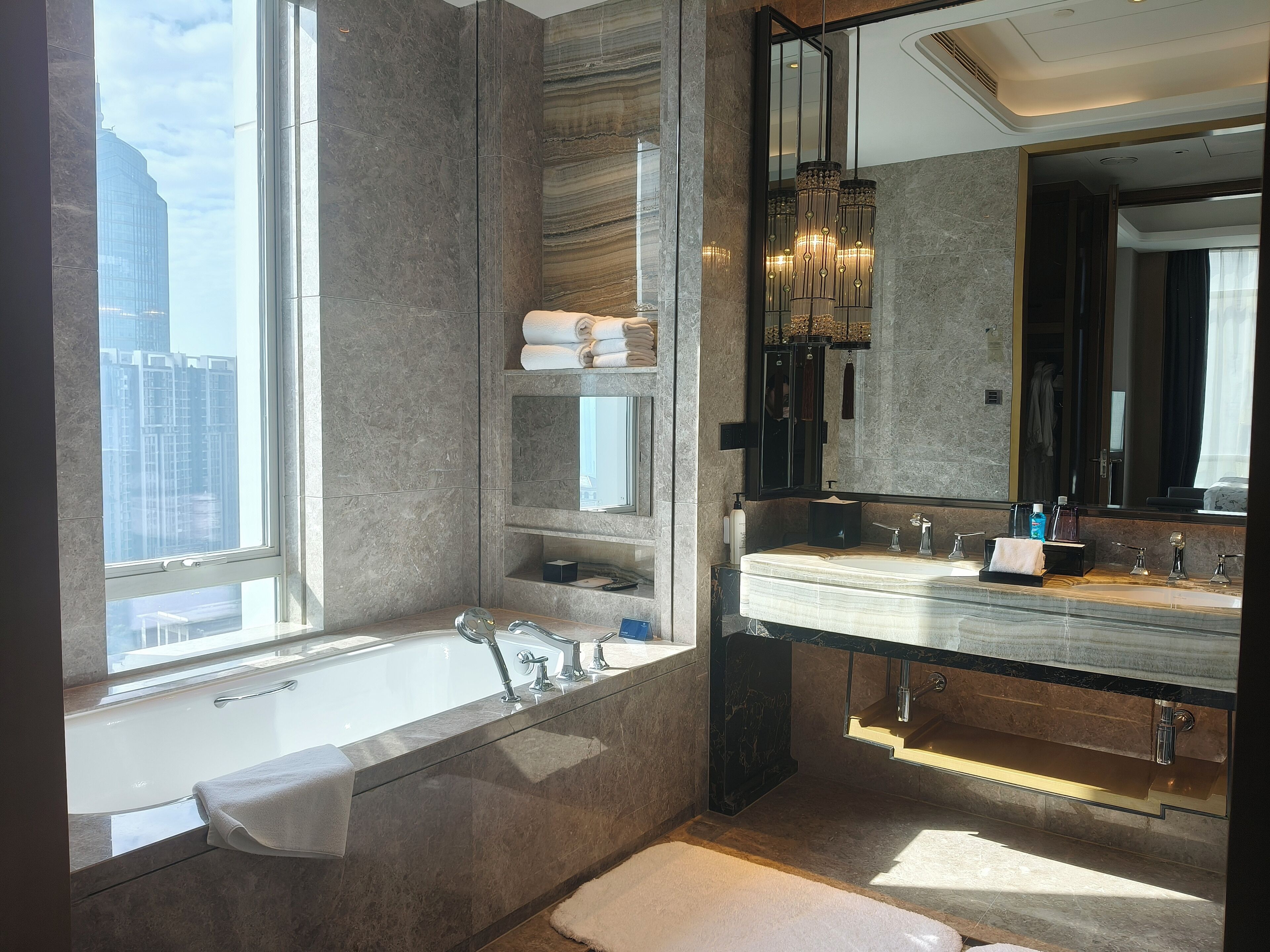 A modern bathroom with a large bathtub, a vanity with a mirror, and a view of tall buildings outside.
