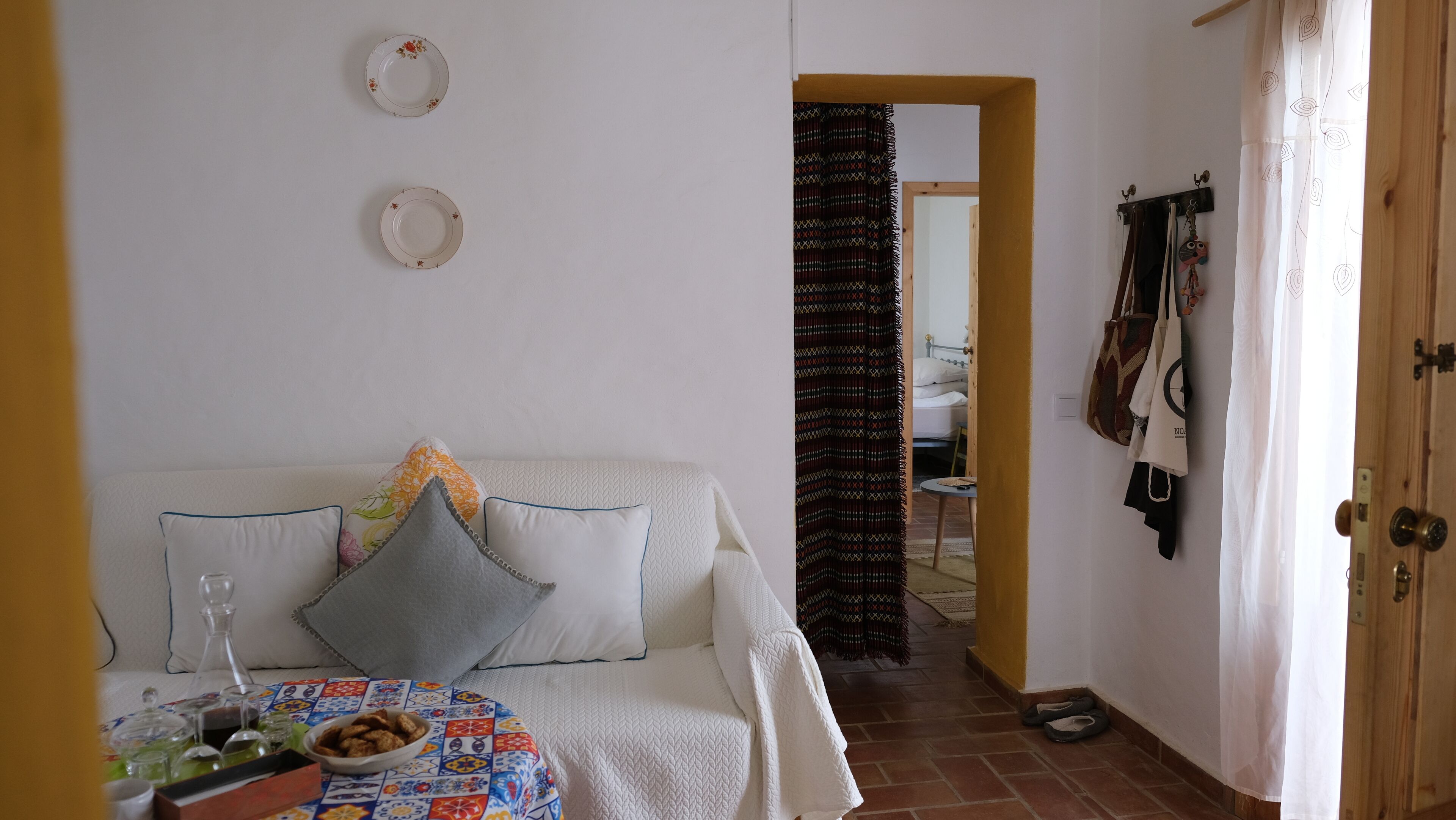 A cozy room with a bed, a table with a bowl of snacks, and a view into another room.