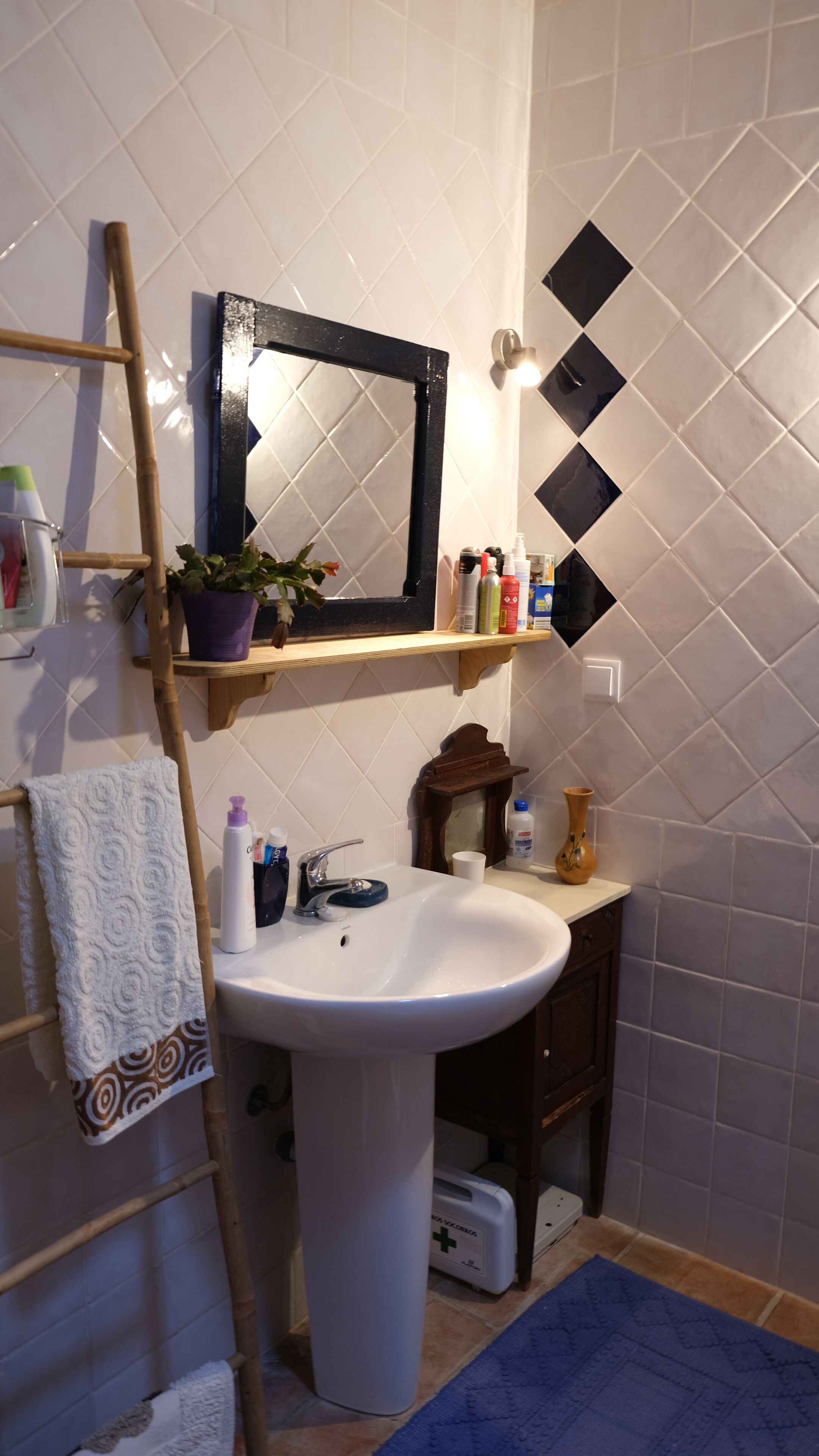 Un baño con un lavamanos blanco, un espejo, un estante con artículos de aseo y un tapete azul en el suelo.