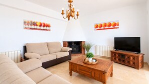 Un salon comprenant un canapé, une table basse, une cheminée, un téléviseur et des œuvres d’art accrochées aux murs.