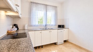 Une cuisine avec des meubles blancs, un plan de travail en granit, une cuisinière noire et une fenêtre ornée de rideaux légers.