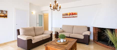 A living room with two sofas, a wooden coffee table, a fireplace, and wall-mounted artwork.