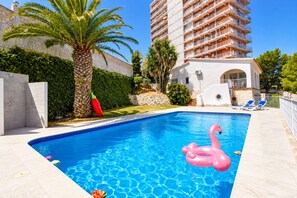 Une piscine avec un flotteur en forme de flamant rose, un palmier et un grand immeuble en arrière-plan.