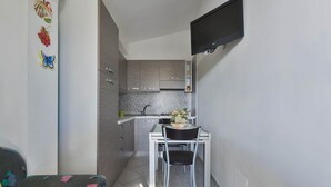 A compact kitchen with a dining area, a flat-screen TV mounted on the wall, and a small table with chairs.