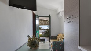 A compact living space with a glass table, a sofa with patterned cushions, and a TV mounted on the wall.