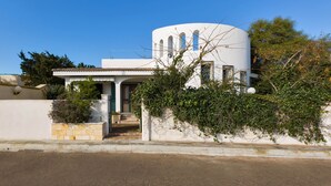 A white building with a curved roof and arched windows, surrounded by greenery.