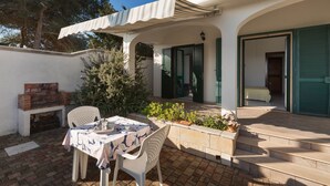 A patio with a table and chairs, a brick fireplace, and a covered area with a striped awning.