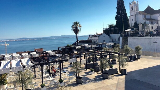 An outdoor seating area with tables and chairs, overlooking a body of water and a coastal town. - I-Centre of old Lisbon in first floor (Lisboa)