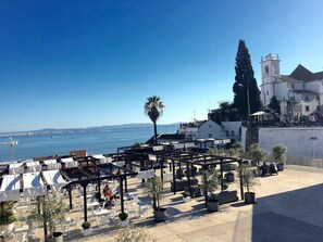 An outdoor seating area with tables and chairs, overlooking a body of water and a coastal cityscape. - I-Centre of old Lisbon in first floor (Lisboa)