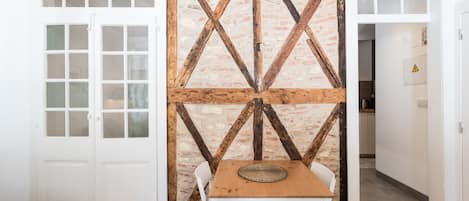 A room with a wooden table and chairs, a white door, and a brick-patterned wall with wooden beams.