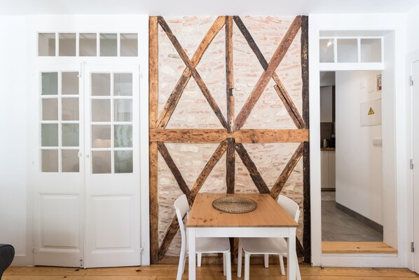 A room with a wooden table and chairs, a white door, and a brick-patterned wall with wooden beams.