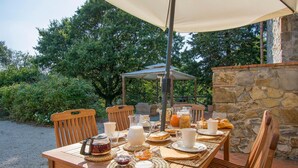 Un espace de restauration en plein air avec une table dressée pour le petit-déjeuner, entouré de murs en pierre et de verdure.