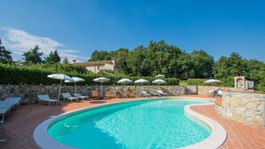 Une piscine entourée de murs de pierre et de verdure, avec des chaises longues et des parasols.