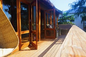 A wooden deck with a wicker chair and a glass door leading to a room. - Casa Algodoal (Tofo)