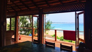 A wooden deck with a table and chairs, overlooking a beach and ocean. - Casa Algodoal (Tofo)