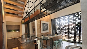 A modern kitchen with a glass partition, a coffee machine, and a seating area with a patterned rug.