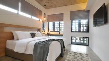 A modern bedroom with a large bed, a ceiling fan, and large windows with a view of the outdoors.