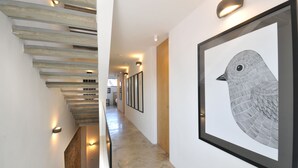 A hallway with a staircase, framed artwork, and wall-mounted lighting.