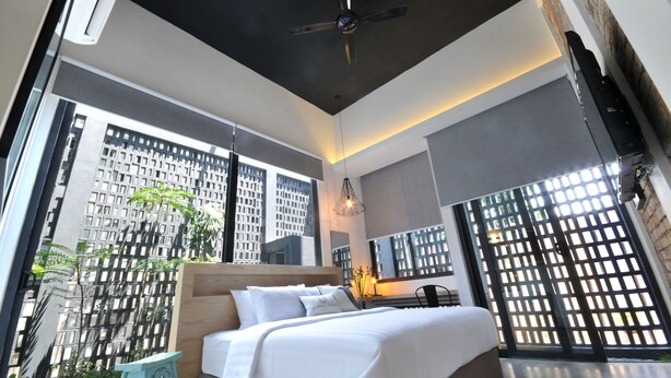 A modern hotel room with a large bed, a ceiling fan, and a view of a cityscape through large windows.