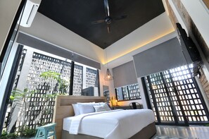 Ett modernt hotellrum med en stor säng, en takfläkt och utsikt över stadsbilden genom stora fönster.