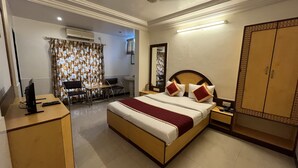 A hotel room with a bed, bedside table, wardrobe, desk with chair, and a bathroom with a mirror and sink. - Hotel Gangasagar (Bengaluru)