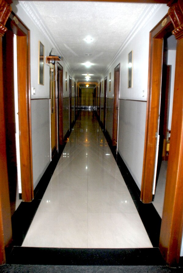 A long, narrow hallway with wooden doors on either side and a shiny tiled floor.