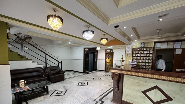 A lobby with a reception desk, a sofa, a coffee table, and a chandelier. - Hotel Gangasagar (Bengaluru)