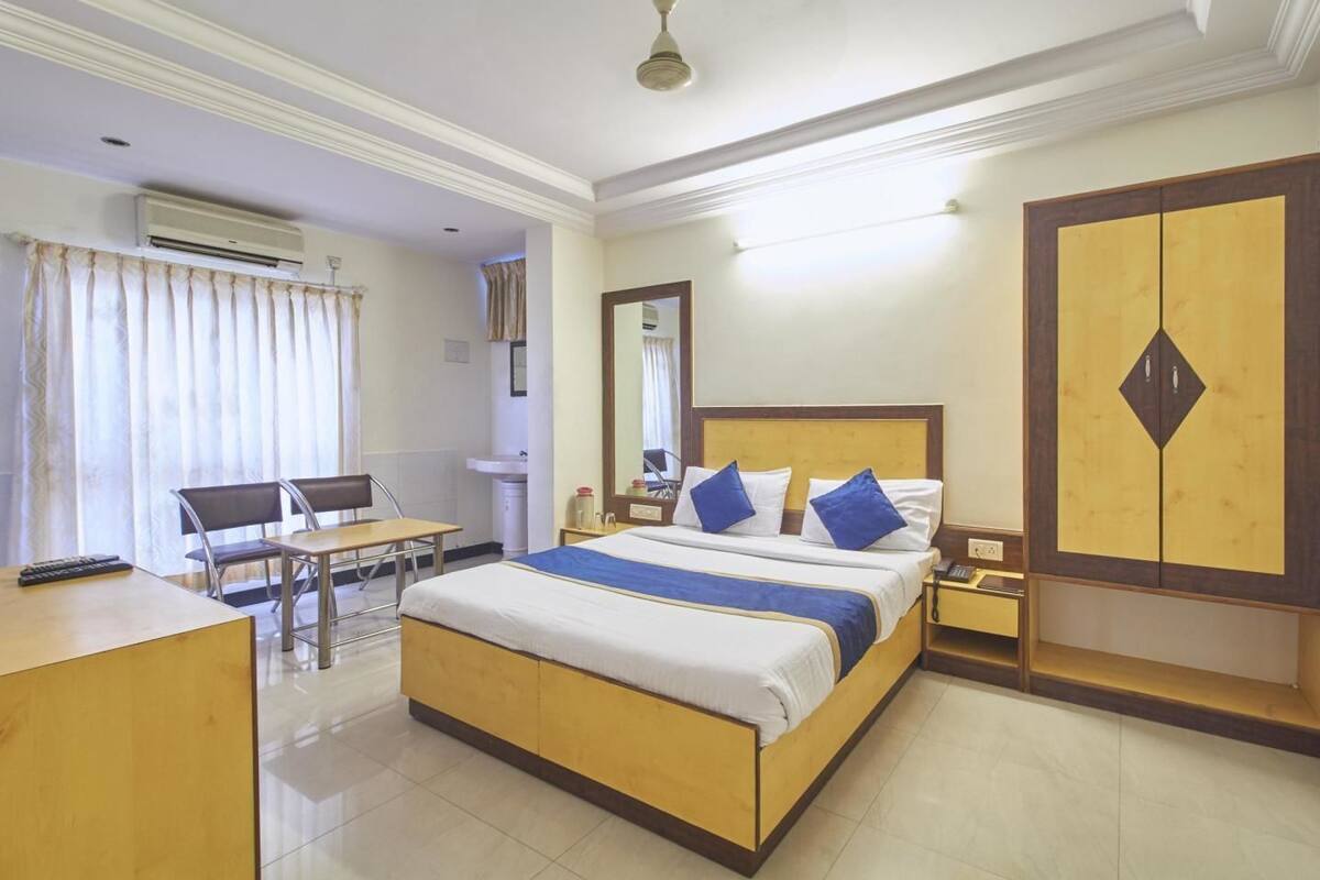 Una habitació d'hotel amb un llit, escriptori, cadira, armari i aire condicionat.