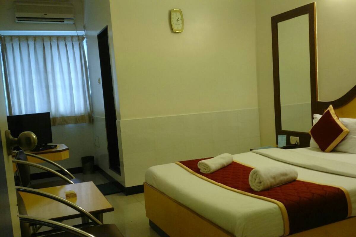 Una habitació d'hotel amb un llit, escriptori, cadira, televisió i mirall.