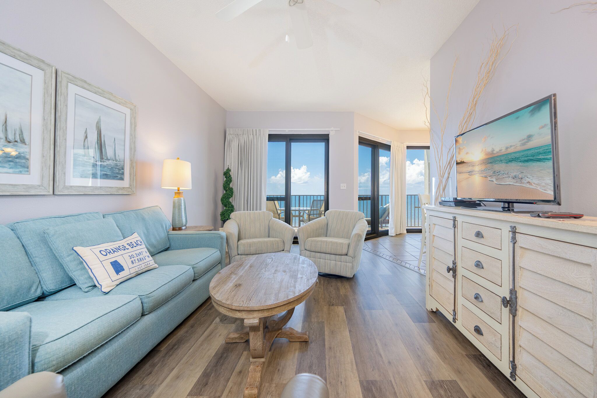 A living room with a sofa, two armchairs, a coffee table, a TV, and a balcony with a view.