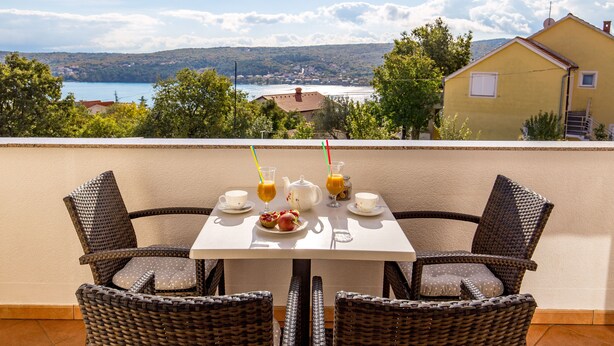A dining table with wicker chairs, a white tablecloth, and a scenic view of a lake and mountains in the background. - Enjoy the sea view | Modern apartment in the idyllic Cizici contact with the owner (Dobrinj)