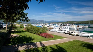 A marina with multiple boats docked, a clear sky, and a grassy area with a pathway. - Enjoy the sea view | Modern apartment in the idyllic Cizici contact with the owner (Dobrinj)